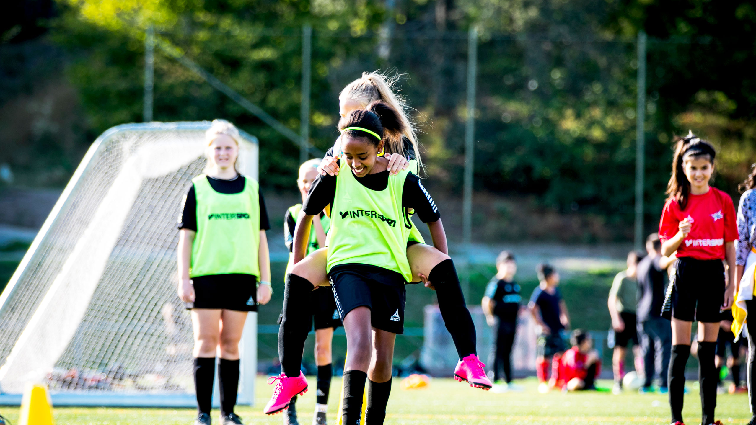 Glada tjejer i 12-årsåldern spelar fotboll på Farsta IP.